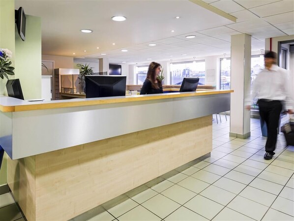 A reception area with a modern desk, two computer monitors, and a large window offering a city view.