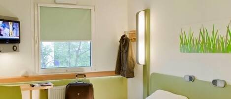 Una habitación de hotel con cama, sillón, televisor, ventana y un cuadro en la pared.