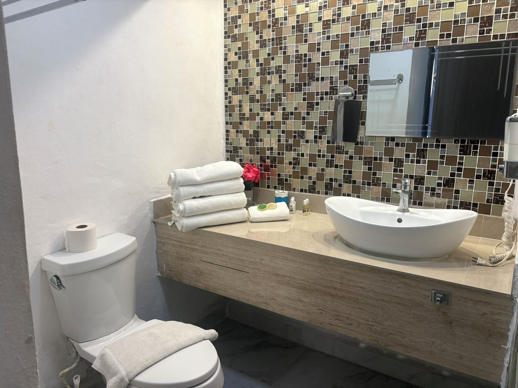 A bathroom with a white toilet, a beige sink, and a tiled backsplash.