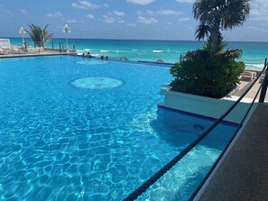 A clear blue pool with a circular design in the center, surrounded by lounge chairs and a view of the ocean. - Cancun Plaza Condo Mexico (Cancun)