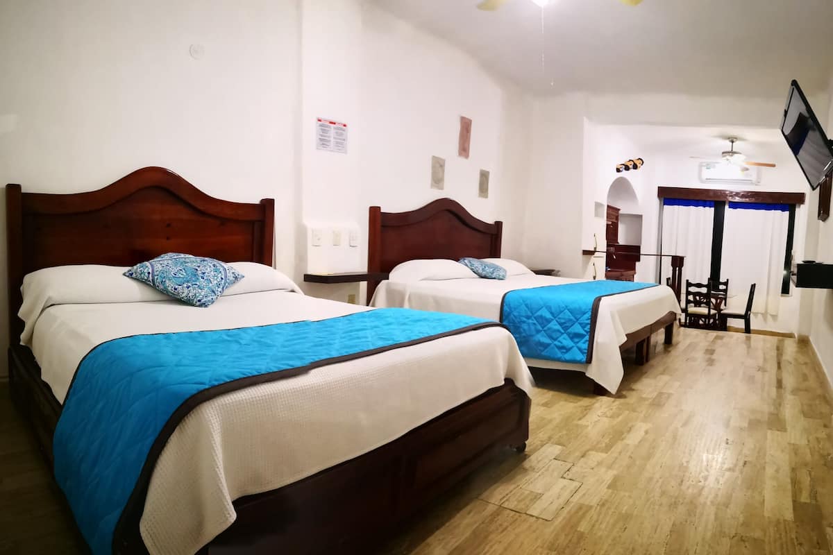 A hotel room with two beds, wooden headboards, white bedding, and a blue quilt.