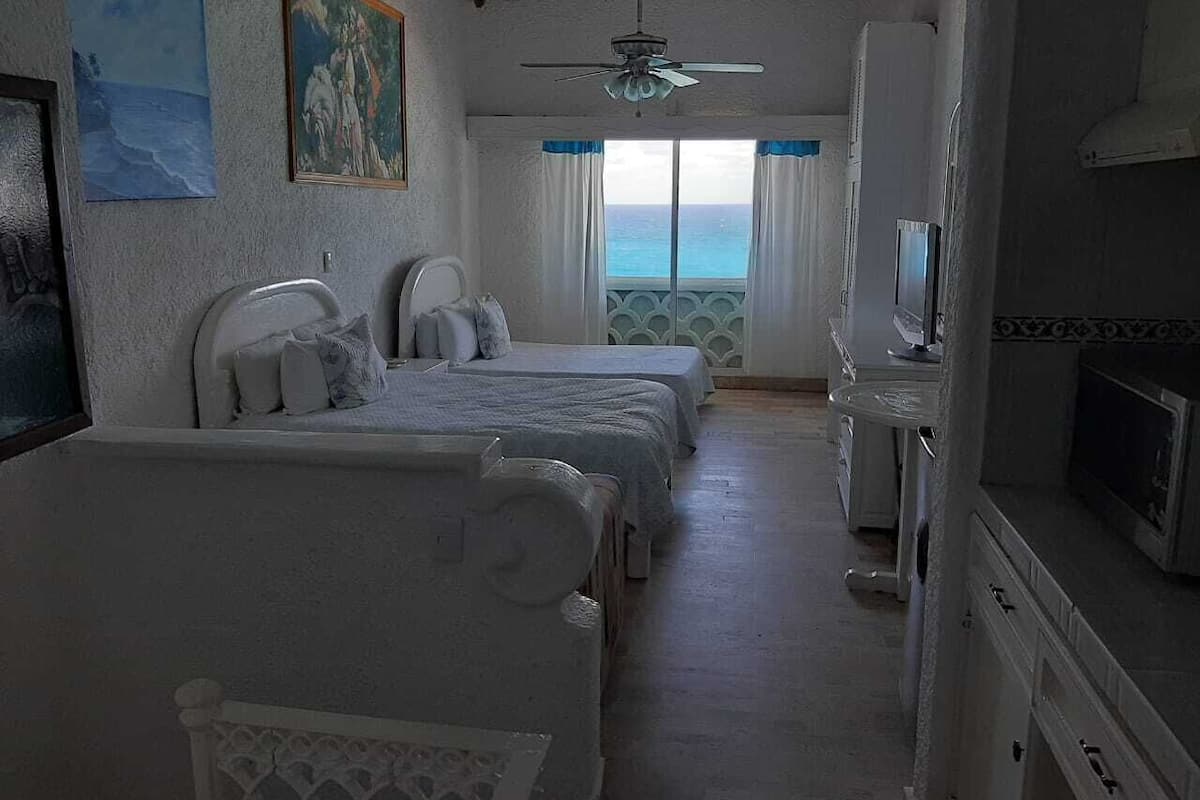 A hotel room with three beds, a ceiling fan, a TV, and a view of the ocean.