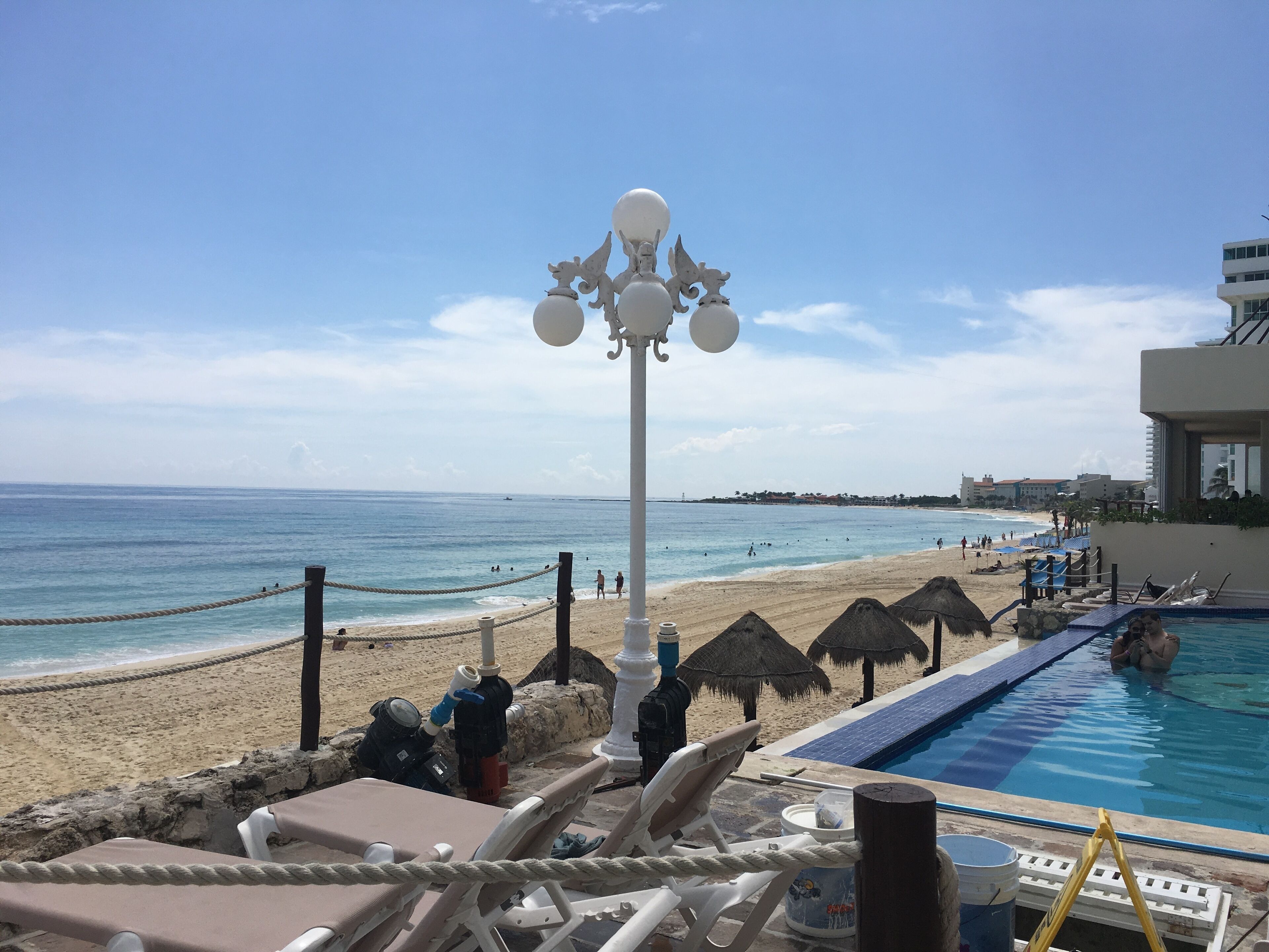 A beachside pool area with lounge chairs, a pool, and a view of the ocean.