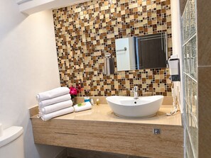 Une salle de bain avec un lavabo blanc, un miroir et un mur recouvert de carreaux.
