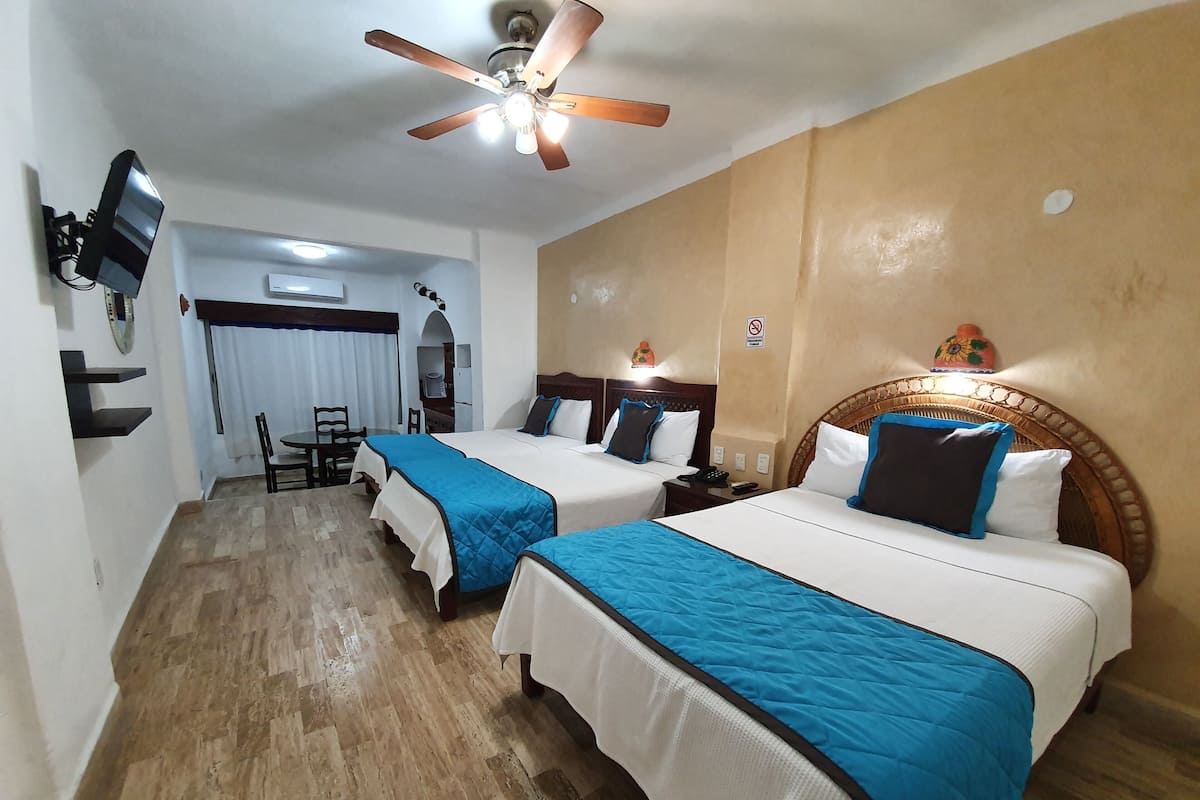 A hotel room with two beds, a ceiling fan, a TV, and a dining area with chairs and a table.