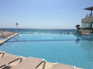 A pool with clear blue water, lounge chairs, and a view of the ocean. - Cancun Plaza Condo Mexico (Cancun)
