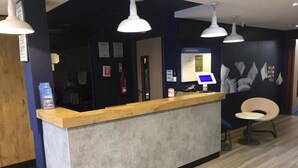 Un mostrador de recepción con encimera de madera y pared gris. Tres lámparas colgantes iluminan el mostrador. Una silla se ve a la derecha.