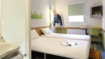 Quarto de hotel com duas camas, banheiro, escrivaninha com computador e televisão.