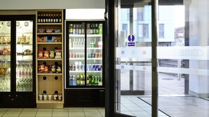 Una tienda con secciones refrigeradas para bebidas y aperitivos, puerta de cristal transparente y suelo de baldosas.