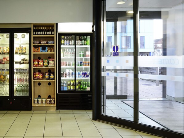 A store with refrigerated sections for beverages and snacks, a clear glass door, and a tiled floor. - ibis budget Portsmouth (Portsmouth)