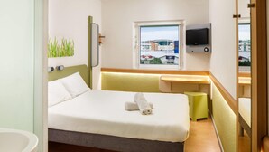Una habitación de hotel con cama, ventana con vista a la ciudad, escritorio y televisión.