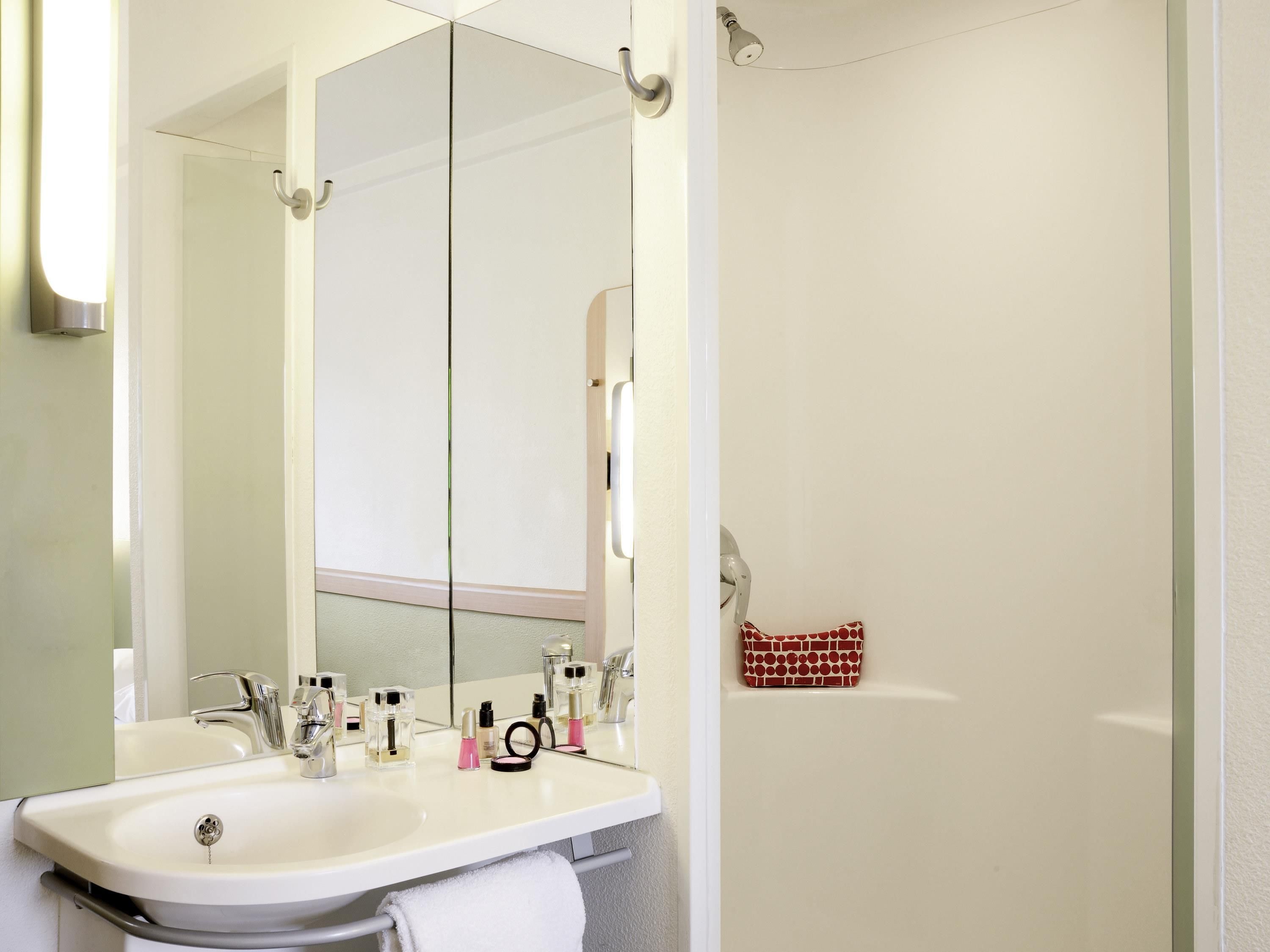 Une salle de bain avec un lavabo blanc, deux robinets, un miroir et un porte-serviettes.