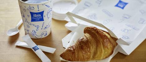 A cup of coffee, a croissant, and a napkin on a wooden table.