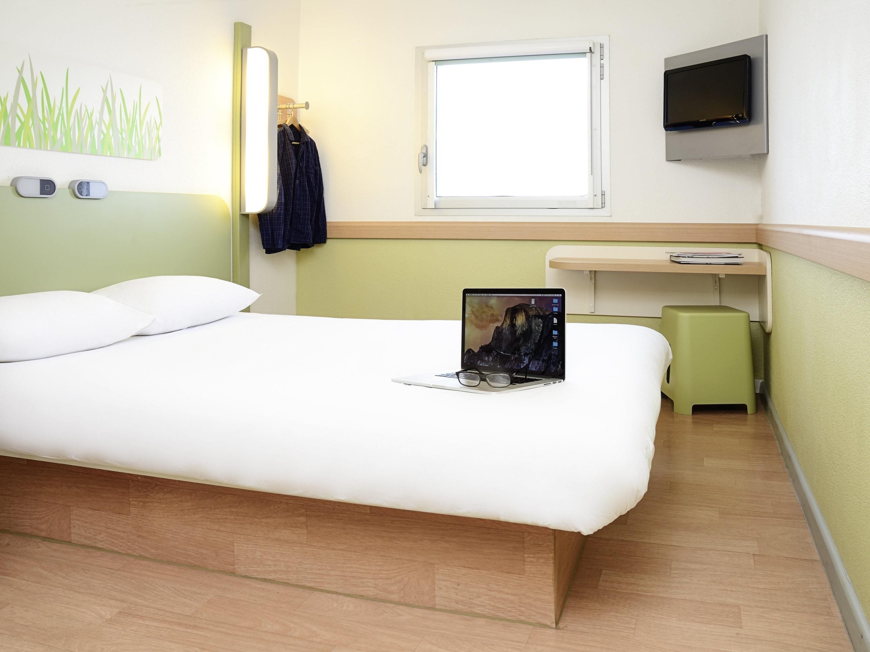 A hotel room with a bed, a desk, a television, and a window.