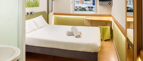 Una habitación de hotel con cama, ventana con vista a la ciudad, escritorio y televisión.