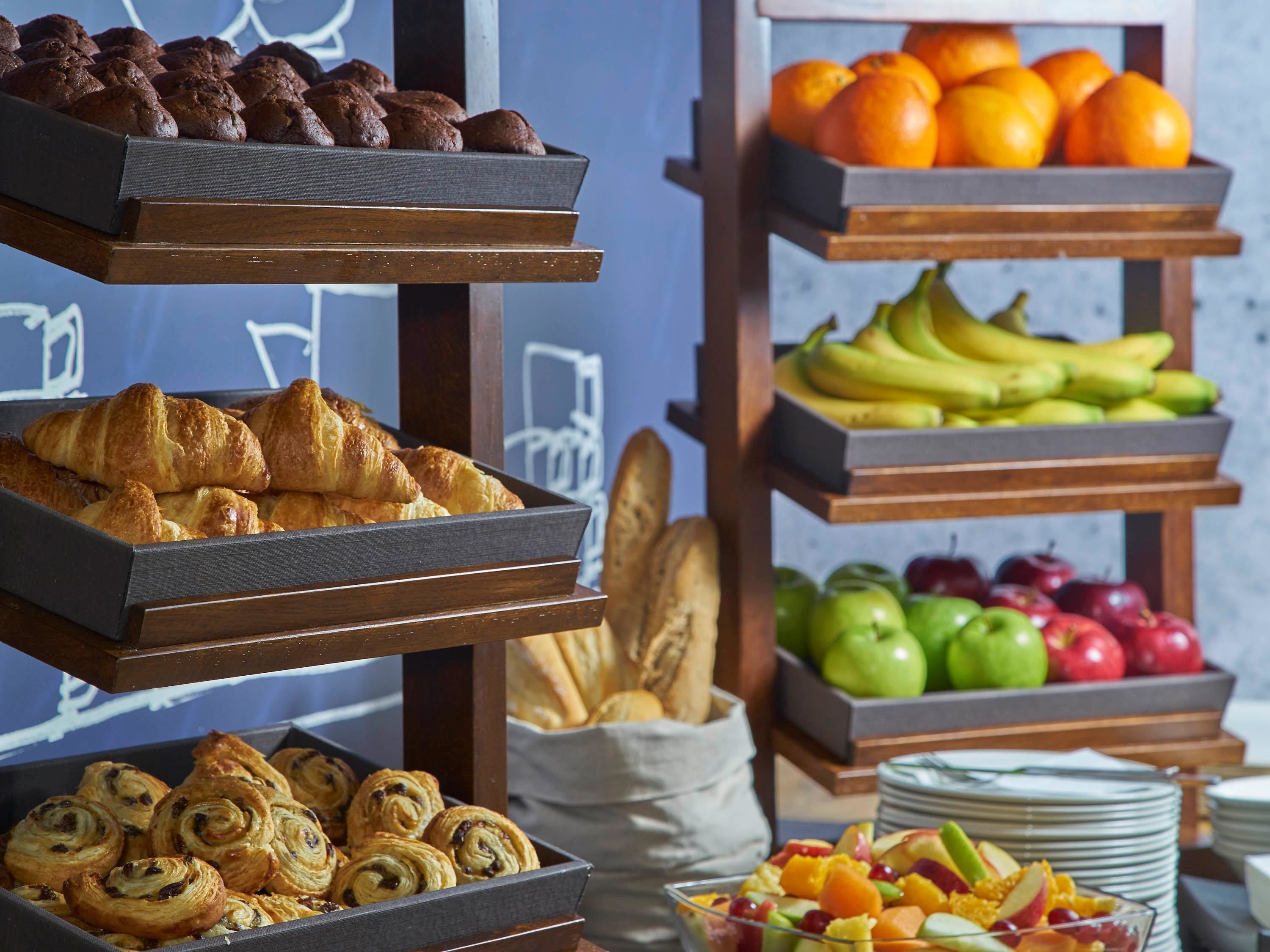 A breakfast buffet with pastries, fruits, and bread.