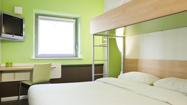 Habitación de hotel con cama, escritorio, silla, televisor y ventana.