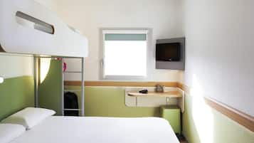 Et hotelværelse med køjeseng, et natbord med lampe, et fjernsyn ophængt på væggen og et vindue der giver naturligt lys.