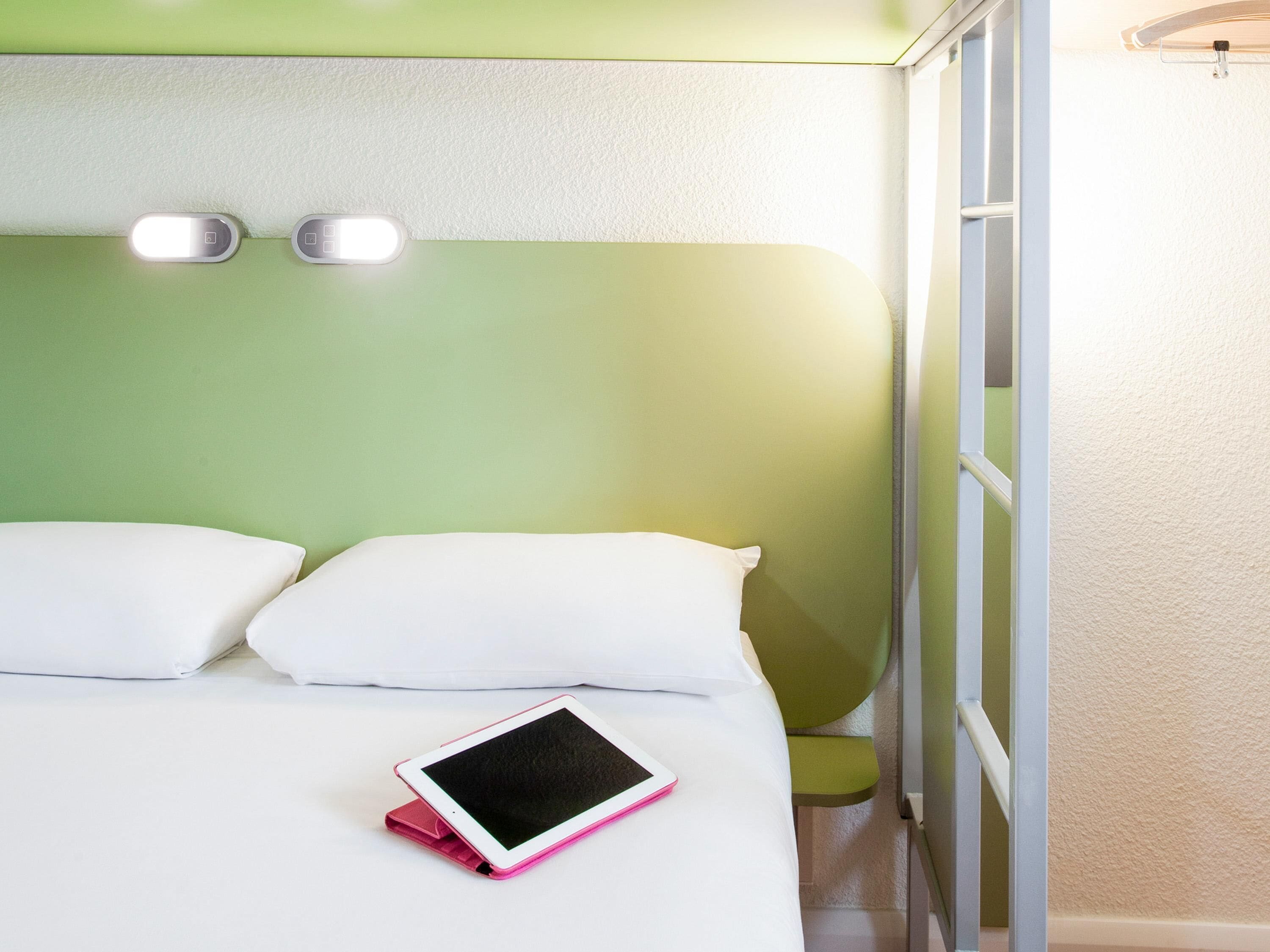 A bed with white bedding, a pink tablet, and two bedside lamps.