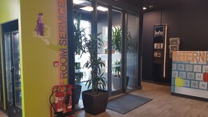 Un área de recepción con un extintor, una planta en maceta y un mostrador de recepción.
