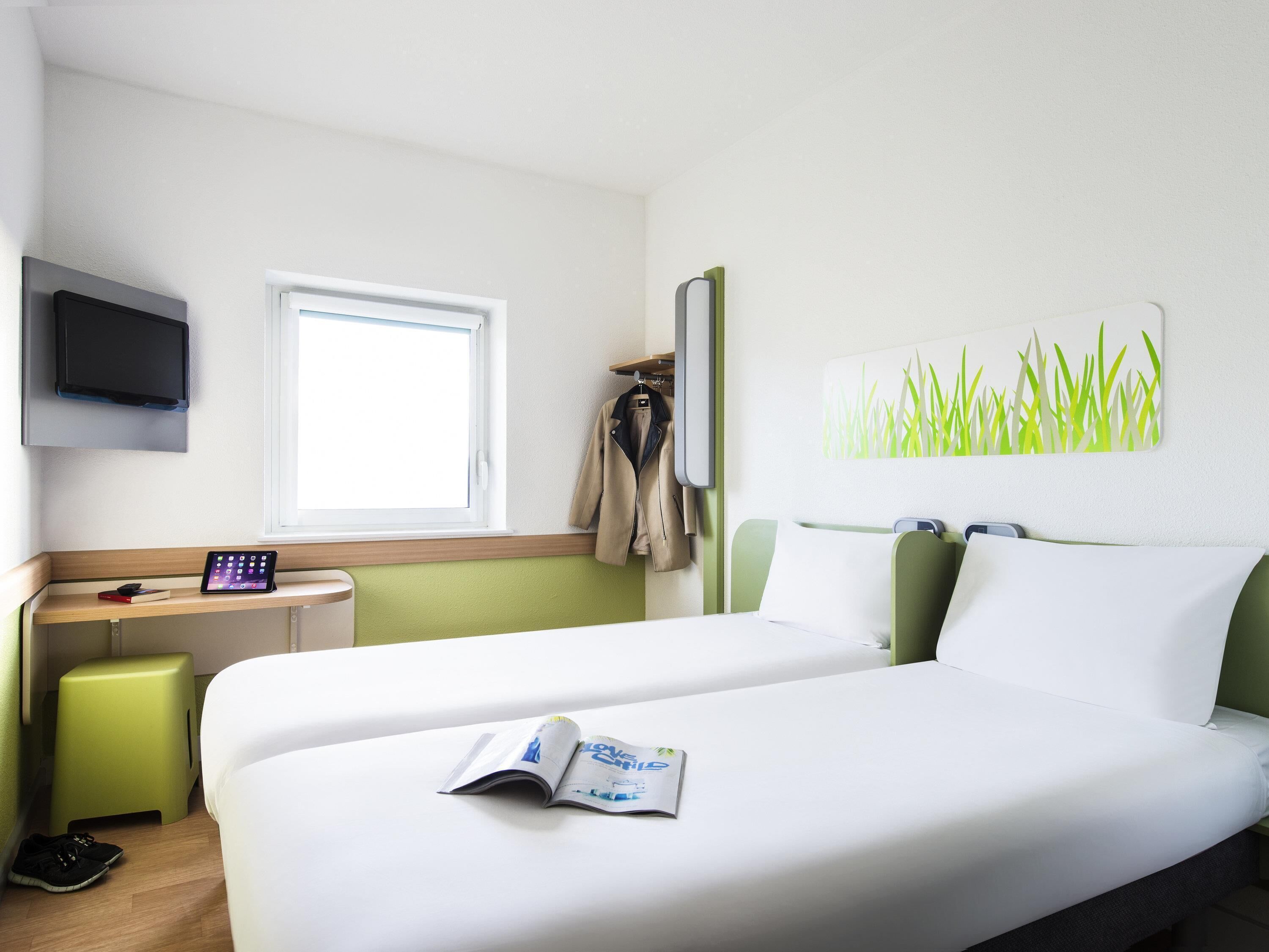 Hotellihuone, jossa on sänky, työpöytä, televisio, ikkuna ja seinätaideteos.