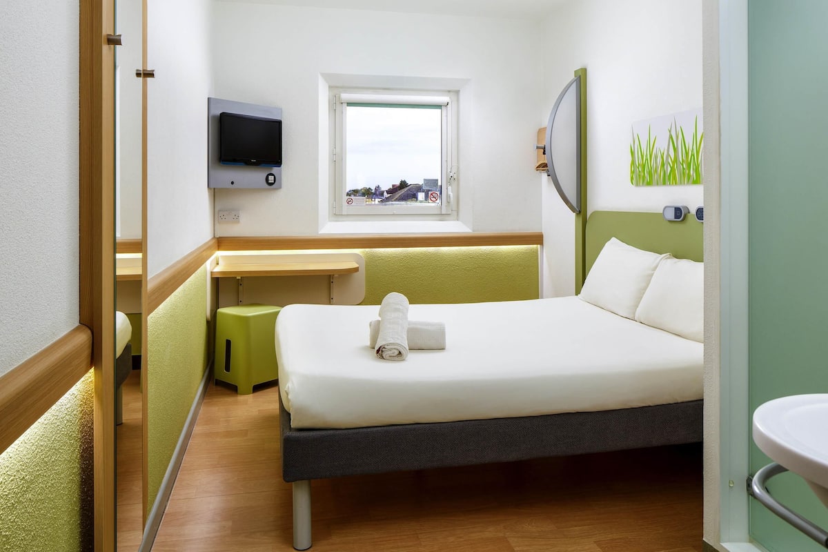 Hotellihuone, jossa on sänky, työpöytä, televisio ja ikkuna, josta on näkymä.