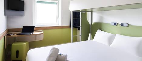 Habitación de hotel con cama, escritorio con computadora portátil, televisor montado en la pared y ventana.