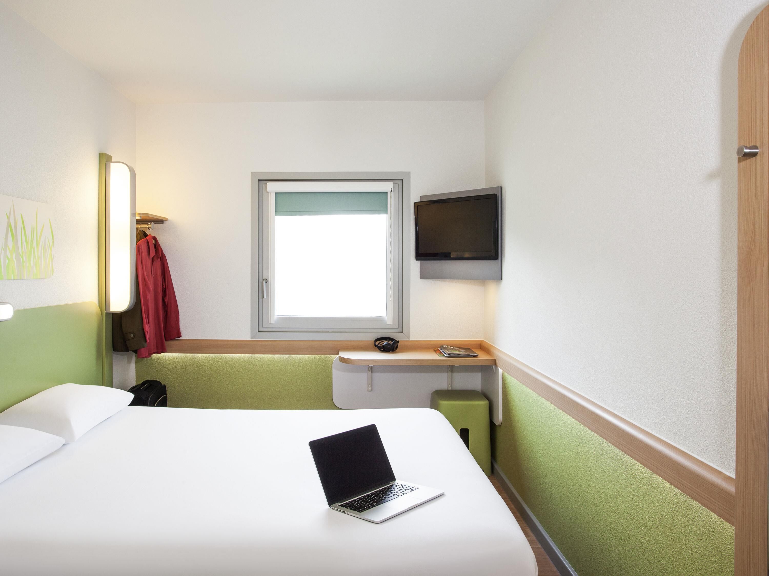 A hotel room with a bed, a desk with a laptop, a television, and a window.
