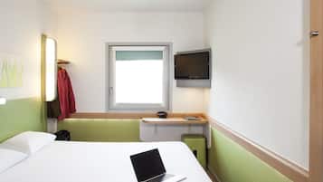 A hotel room with a bed, a desk with a laptop, a television, and a window.