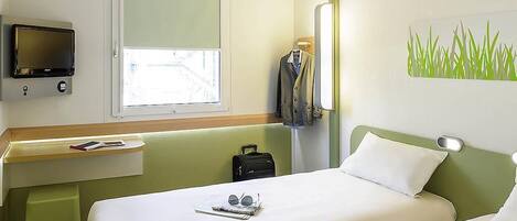 A hotel room with a bed, a desk, a TV, a window, and a wall art piece.