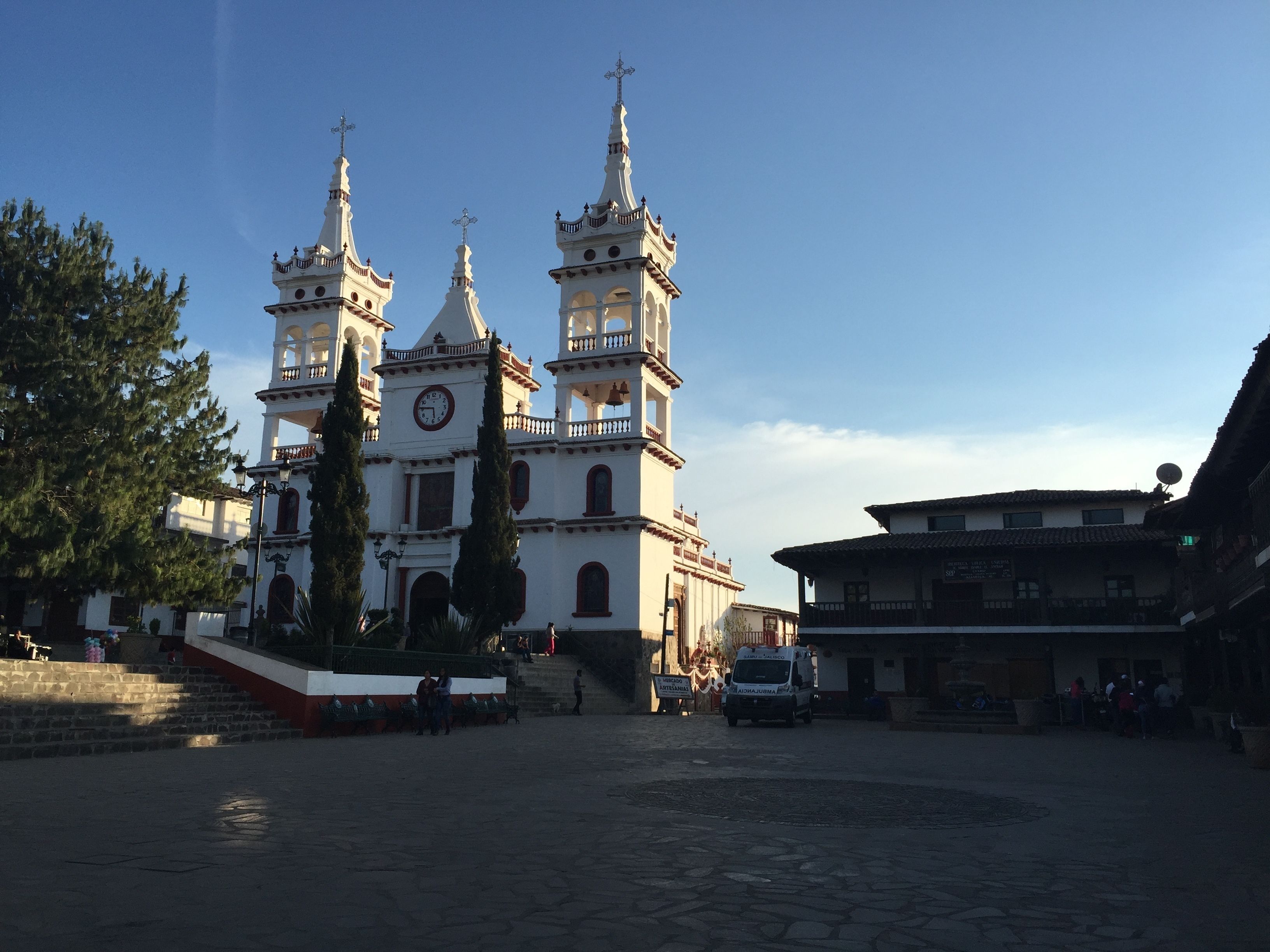 Una iglesia histórica con tres torres y un reloj, rodeada de calles empedradas y edificios tradicionales.