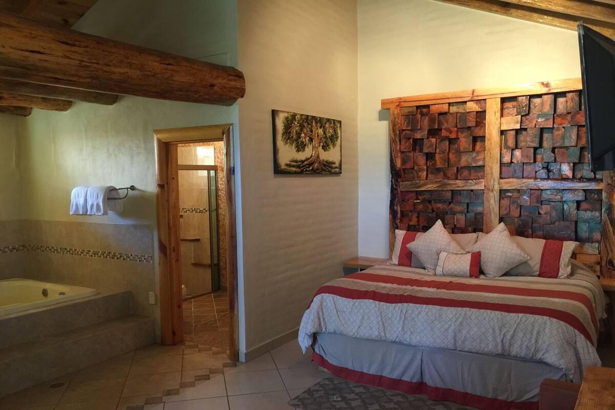 Un dormitorio con una cama grande, un cabecero de madera, un cuadro, y un baño con bañera y ducha.
