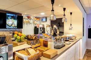 A buffet setup with various food items and beverages, a television screen, and modern lighting fixtures.