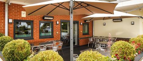 An outdoor seating area with tables and chairs, surrounded by neatly trimmed bushes and flowering plants.