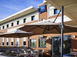 An outdoor seating area with umbrellas, a brick building, and a sign for ibis budget hotels.