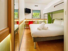 A modern hotel room with a bed, a desk, a chair, and a television.