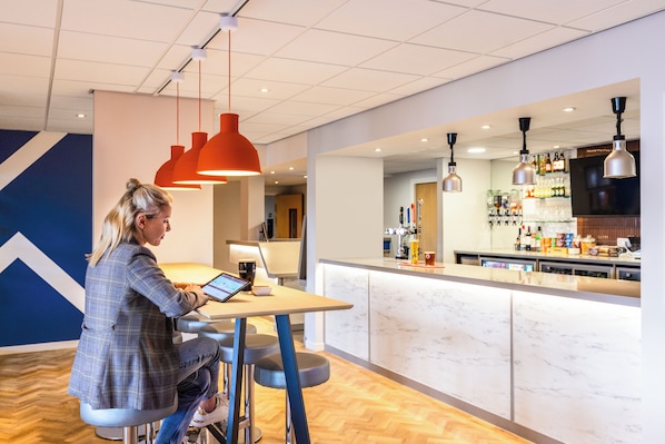 Un interior moderno con una zona de bar, asientos y una persona usando una computadora portátil.