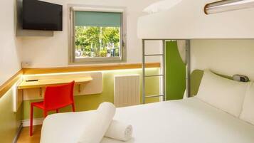 A hotel room with a bunk bed, a desk with a chair, a television, and a window with a view of greenery.
