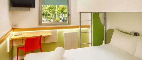 Habitación de hotel con literas, un escritorio con silla, televisión y ventana con vistas a la vegetación.