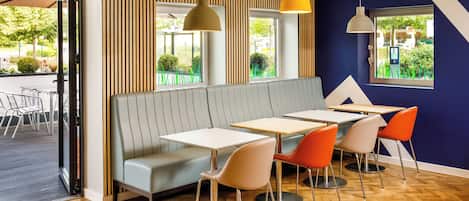 A modern restaurant interior with a wooden herringbone floor, a grey booth seating area, and orange chairs around tables.