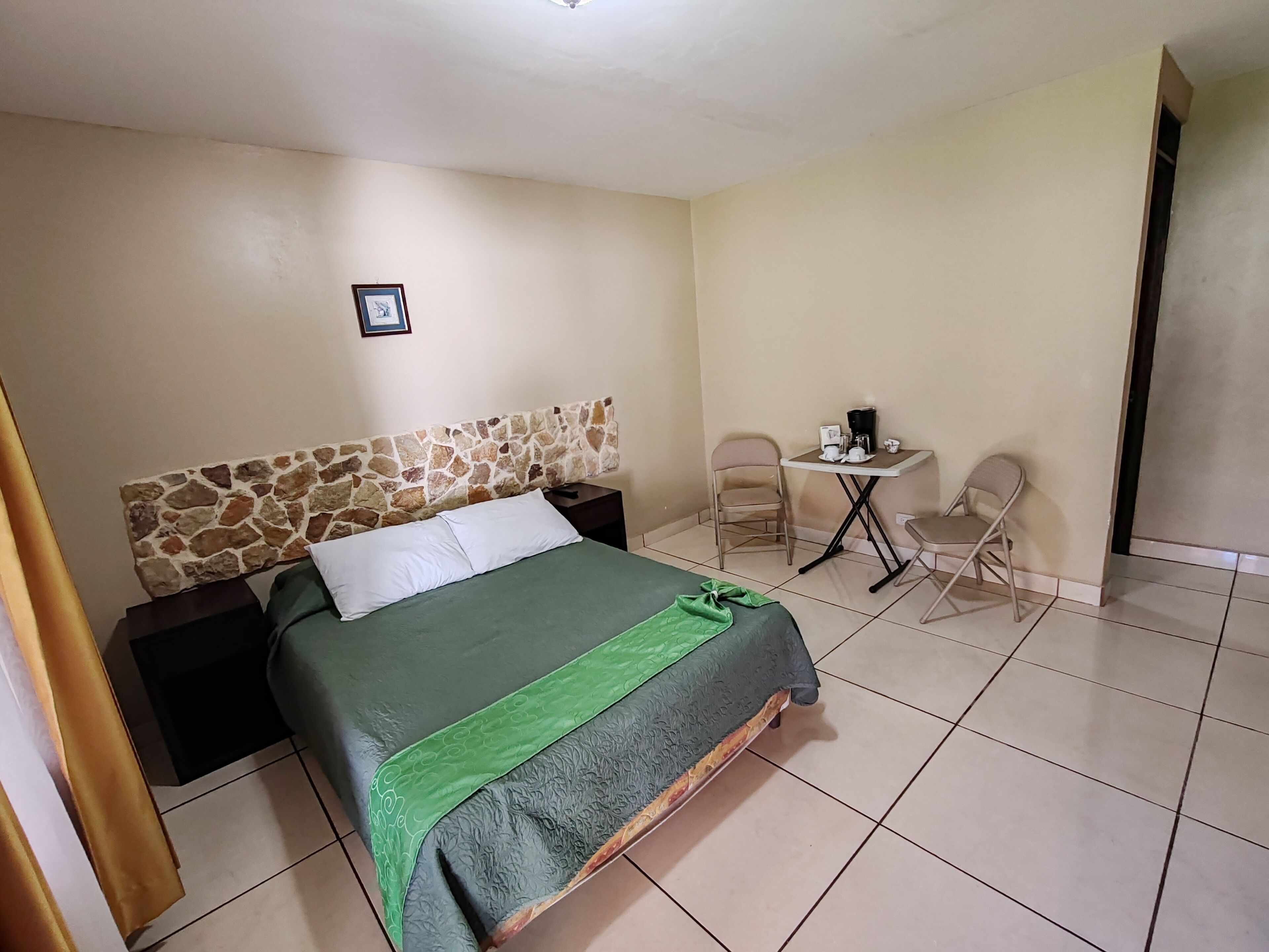 A hotel room with a bed, a small table with chairs, and a stone headboard.