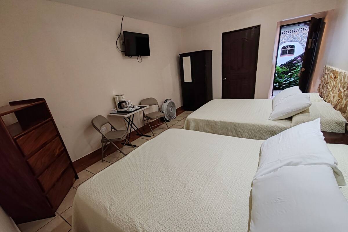 A hotel room with two beds, a desk with a chair, a coffee maker, and a TV mounted on the wall.