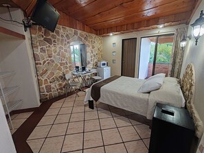 Un dormitorio con pared de piedra, una cama, un escritorio con silla, televisor y ventana con cortinas.