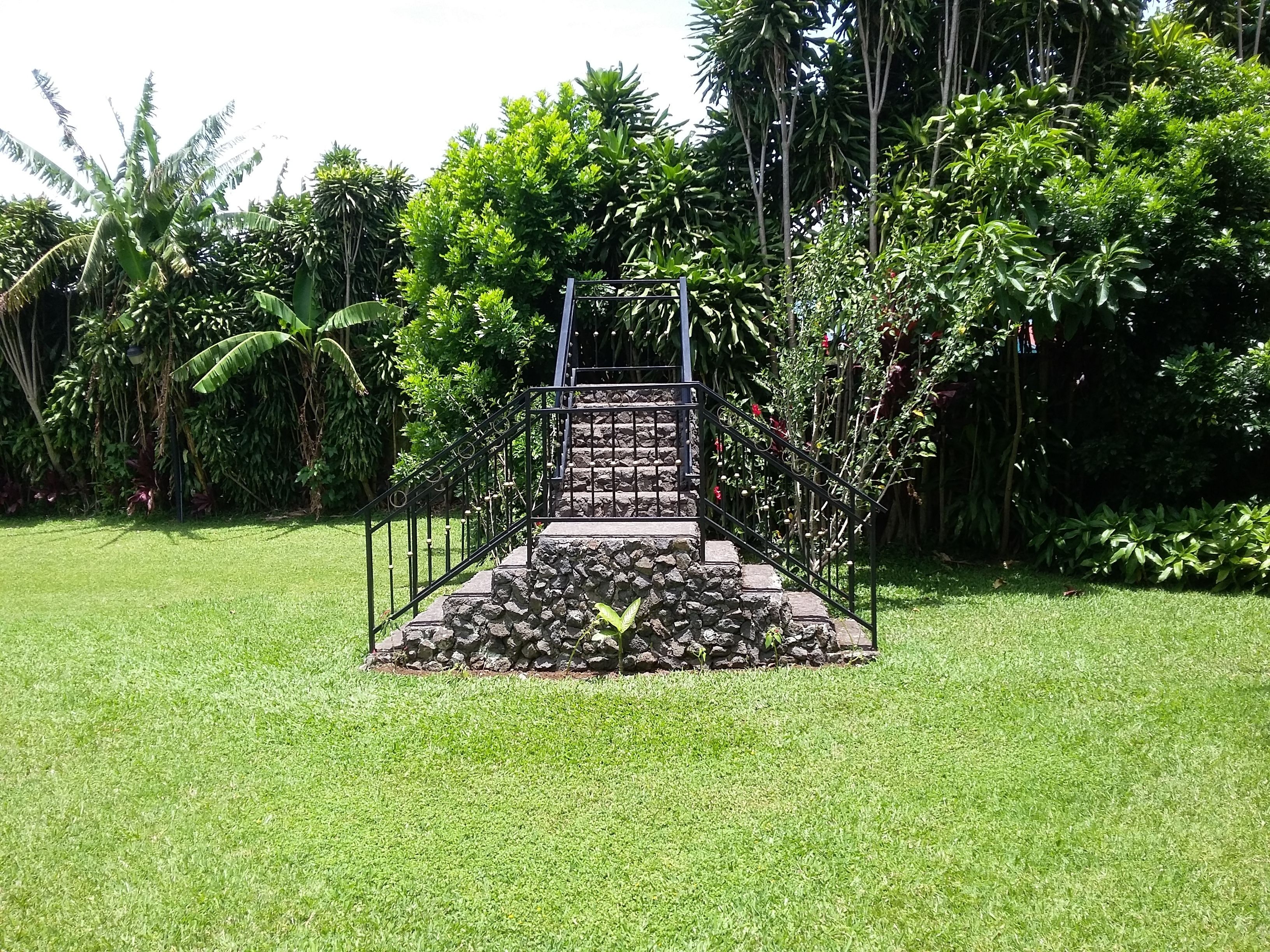 Eine Steintreppe führt zu einem Metallgeländer, umgeben von üppiger Vegetation und Bananenpflanzen.