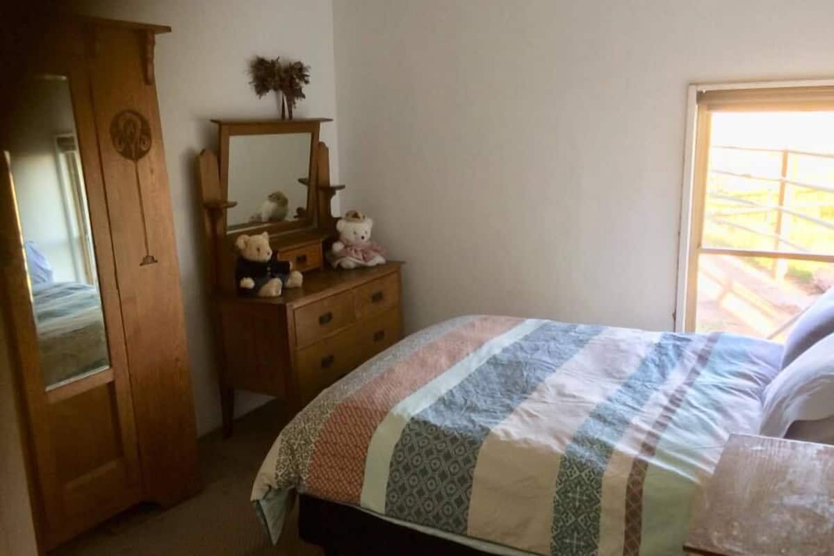 Un dormitorio con cama, cómoda de madera, espejo y ventana.