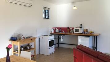 A compact kitchen with a stove, microwave, and sink. There is a wooden table with a vase and a red couch in the foreground.