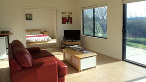 A modern living room with a red sofa, a wooden coffee table, a television, and a large window offering a view of the outdoors. - Abington Farm (Heyfield)