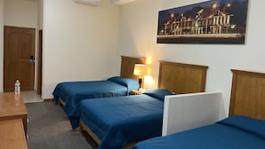 Habitación de hotel con tres camas, un escritorio de madera, una botella de agua, aire acondicionado y un cuadro de un edificio.