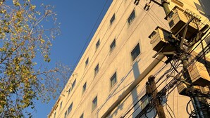 Un edificio de varios pisos con muchas ventanas e infraestructura eléctrica a la vista.