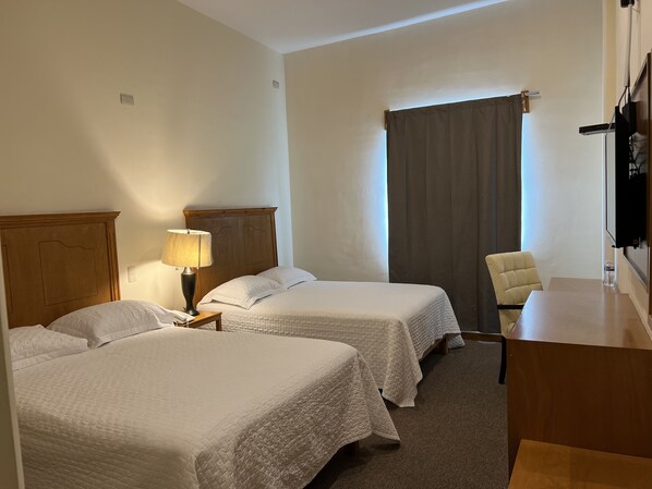 Une chambre d’hôtel avec deux lits, un bureau, une chaise, une lampe et un téléviseur.